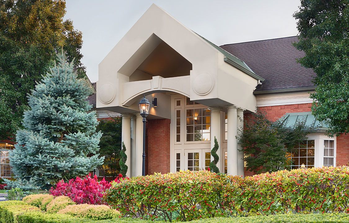 Architectural view of Mcknight Place Assisted Living community with lush trees and portico.