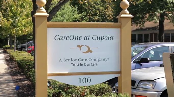Exterior view of CareOne at The Cupola senior living community with sign and greenery.