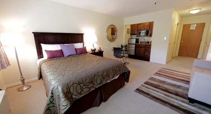Interior design of a cozy bedroom with bed, cushion, lamp, and rug at CareOne at The Cupola senior living community.
