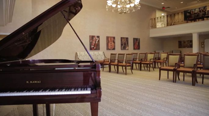 A pianist performing on a grand piano under a chandelier at CareOne at The Cupola Senior Living.