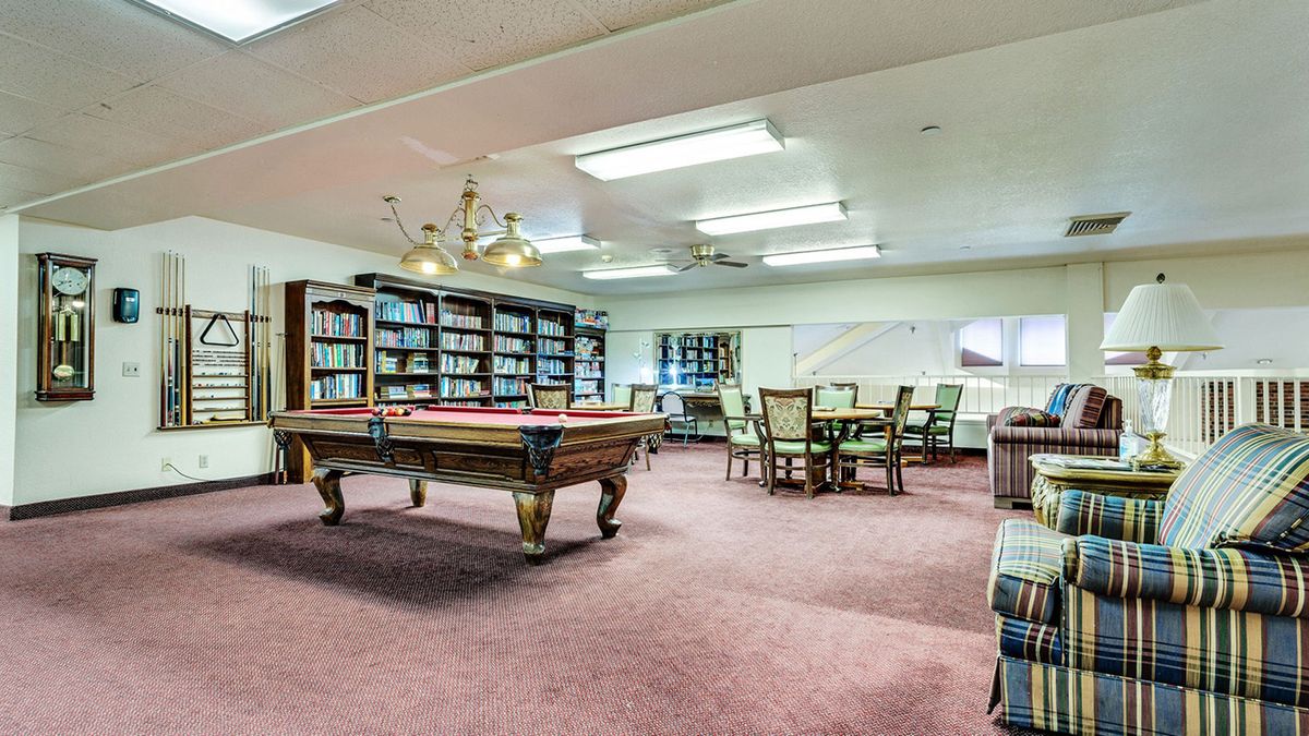Senior living community Country Squire's indoor billiard room with pool table, chairs, and couch.