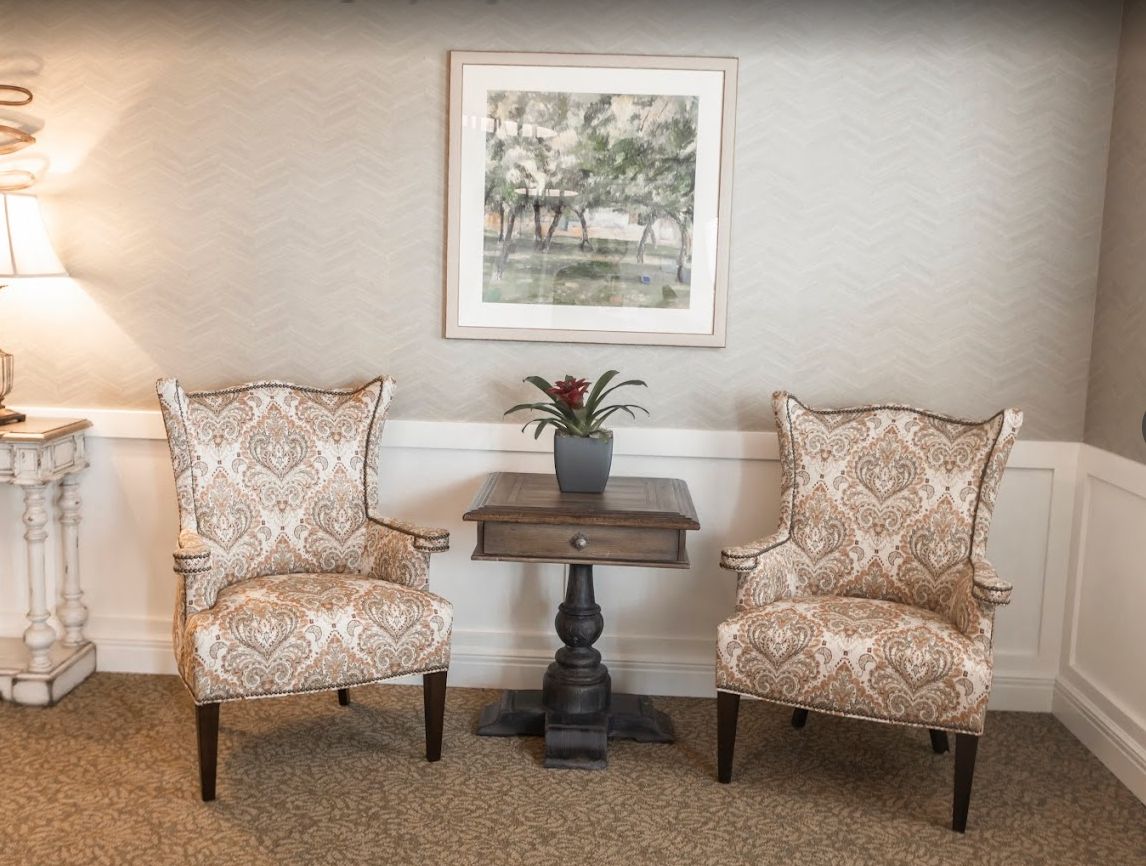Senior living room at The Wildwood, featuring cozy armchairs, decorative pillows, art paintings, and home decor.