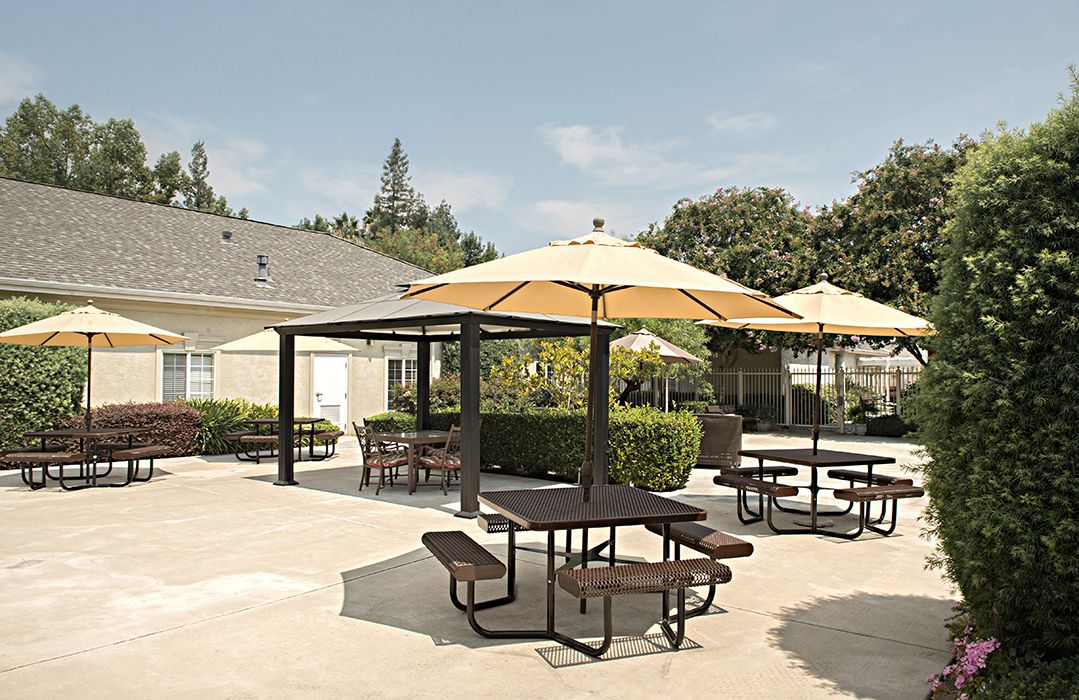 Senior living community with patio furniture, canopy, and lush greenery in a well-architectured building.