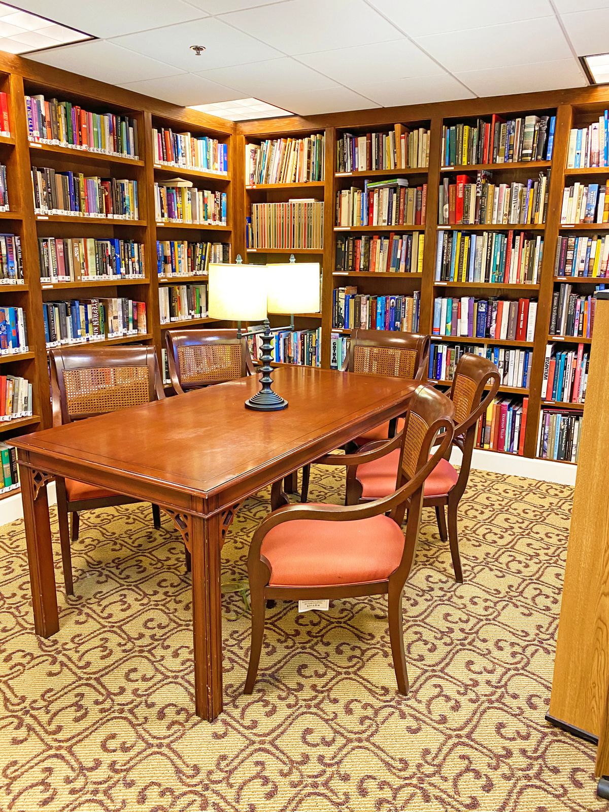 Senior residents enjoying a well-lit library with bookcases, tables, chairs, and desks at AlmaVia of San Francisco.
