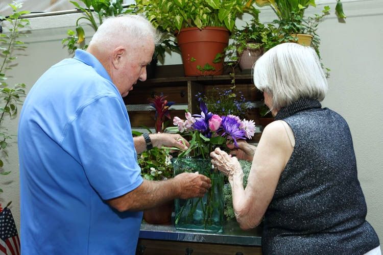 Senior man and woman gardening at 80th Street Residence, surrounded by potted plants and flowers outdoors.