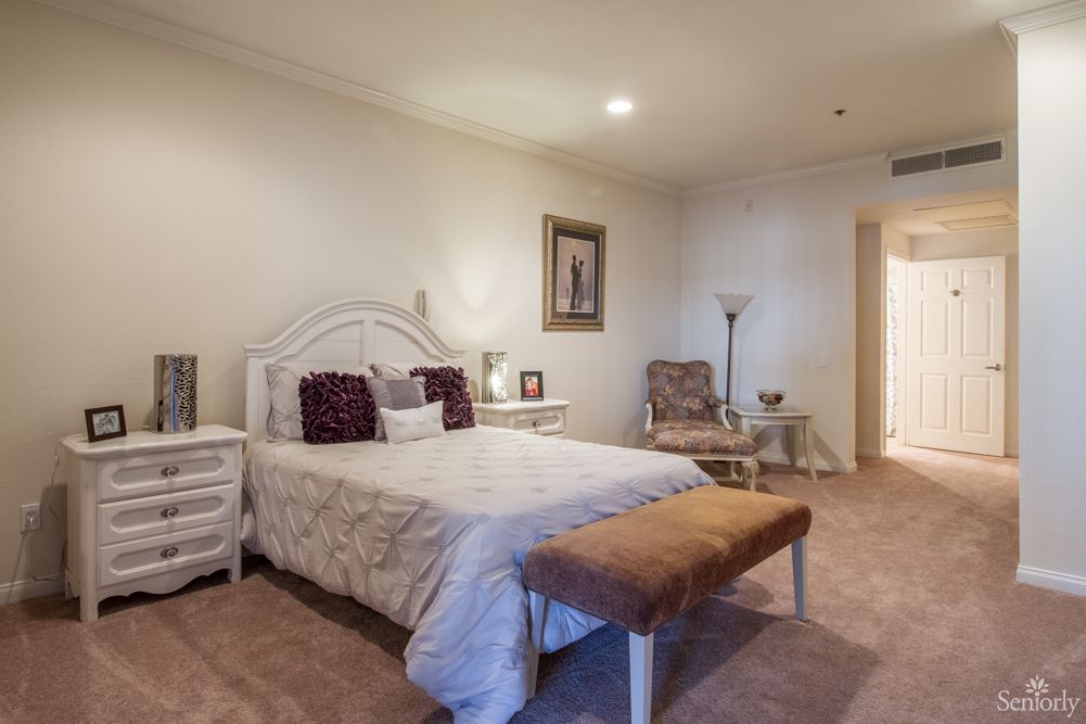 Senior resident relaxing in a well-furnished bedroom at Palm Court senior living community.