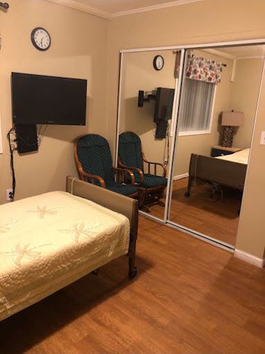 Senior's bedroom at Jewel Lake Assisted Living Home featuring a bed, chair, and computer.