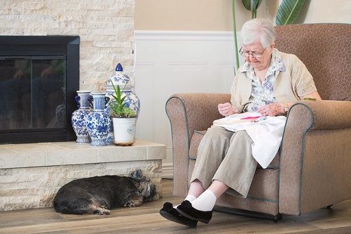 Senior woman with glasses and dog sitting on couch, man in chair by fireplace at Oakdale.