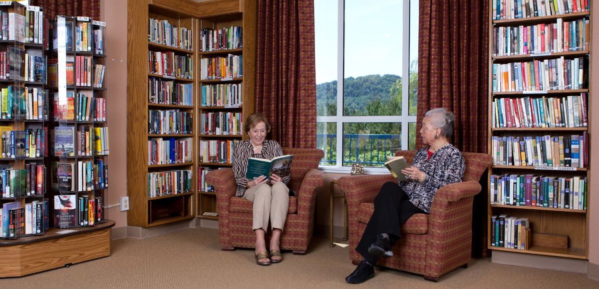 Senior woman reading a book in the library of Villa Marin senior living community.