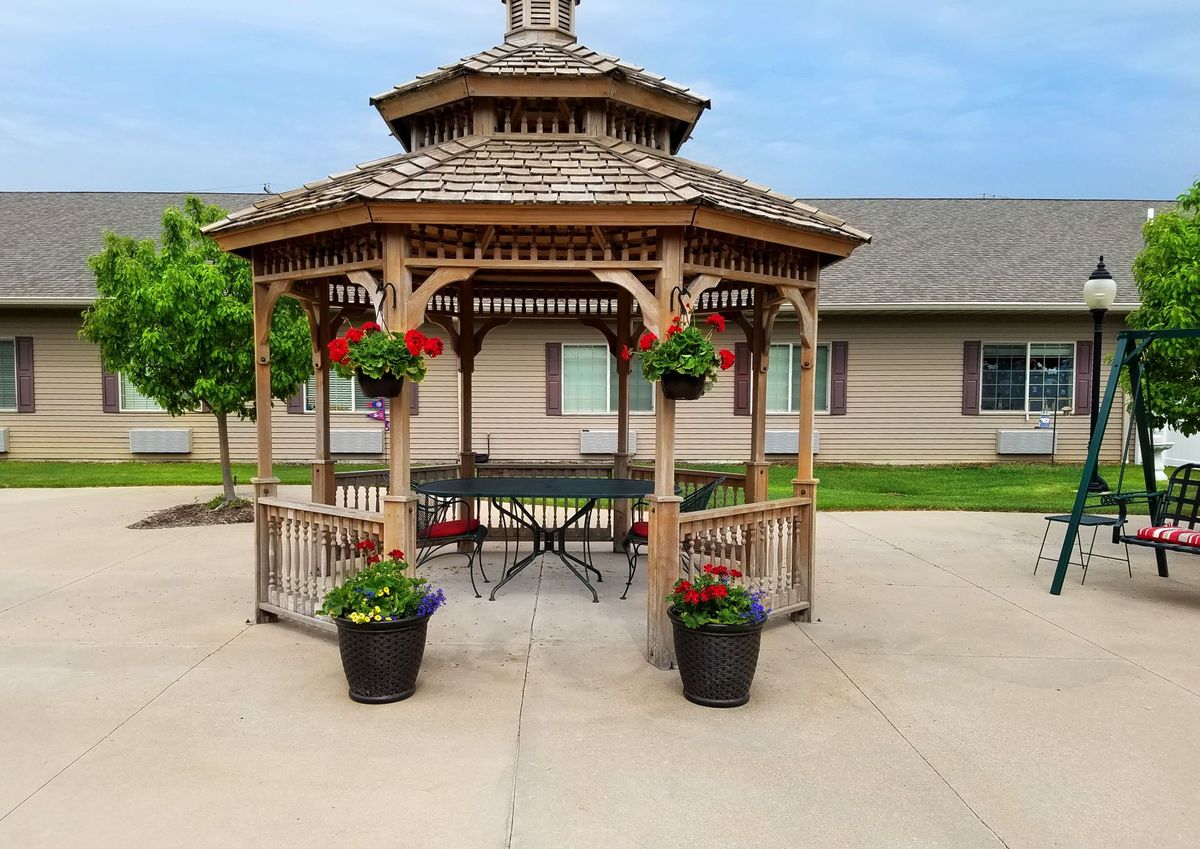 Outdoor view of Courtyard Estates Of Bushnell senior living community featuring a gazebo, yard, and building.