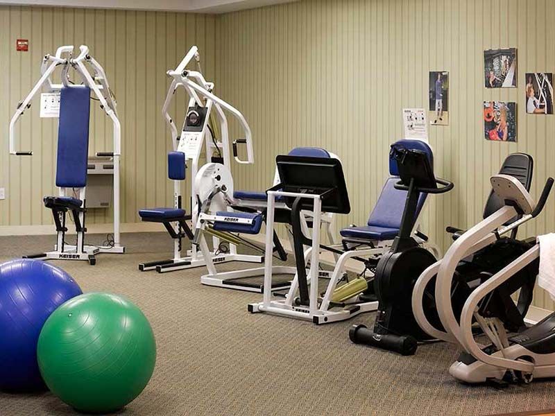 Senior person working out at Atria Lincoln Place gym with fitness accessories and weights.