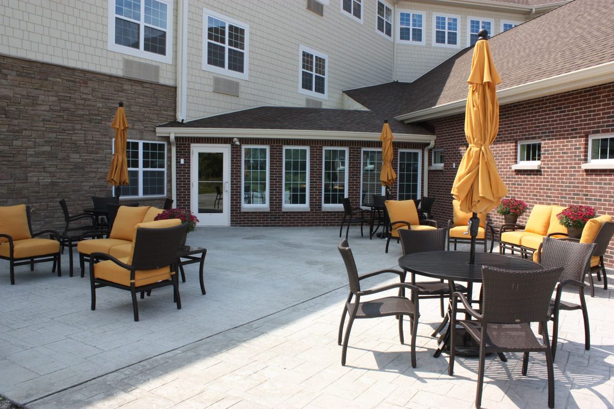Senior living community, Montclare Supportive Living, featuring patio dining, lush backyard, and elegant architecture.