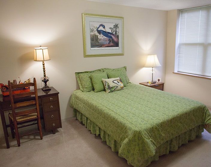 Senior living community bedroom at Ascension Living Bethlehem Woods with bed, chair, and bird decor.