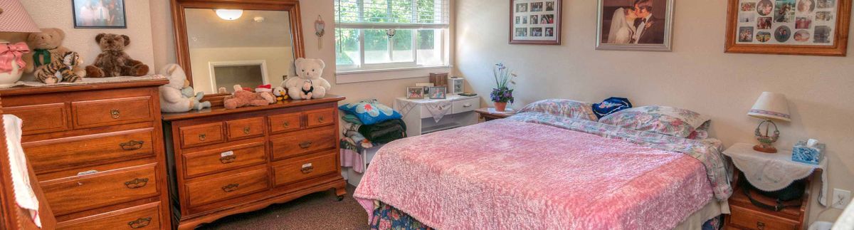 Senior resident in a well-furnished bedroom at Poppy Fields Assisted Living community.