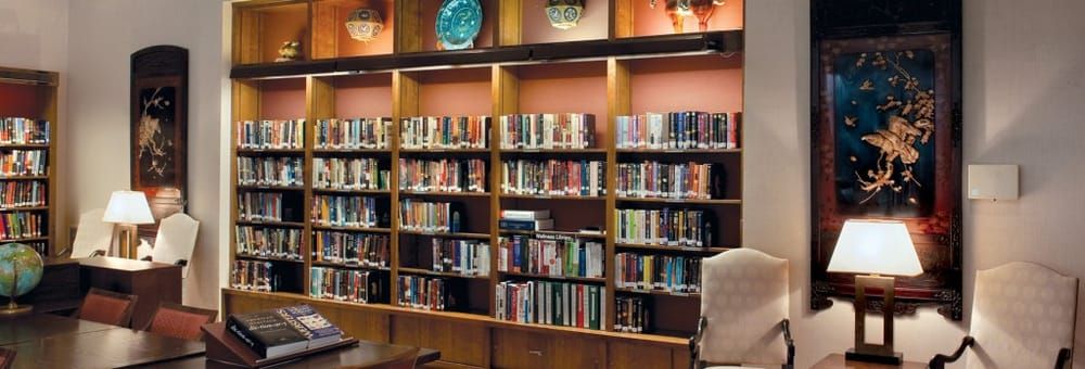 Senior living community library in Los Gatos Meadows with lamp, books, furniture, and art.