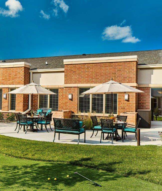 Senior living community, The Sheridan At Green Oaks, featuring a bench, house, and lush greenery.