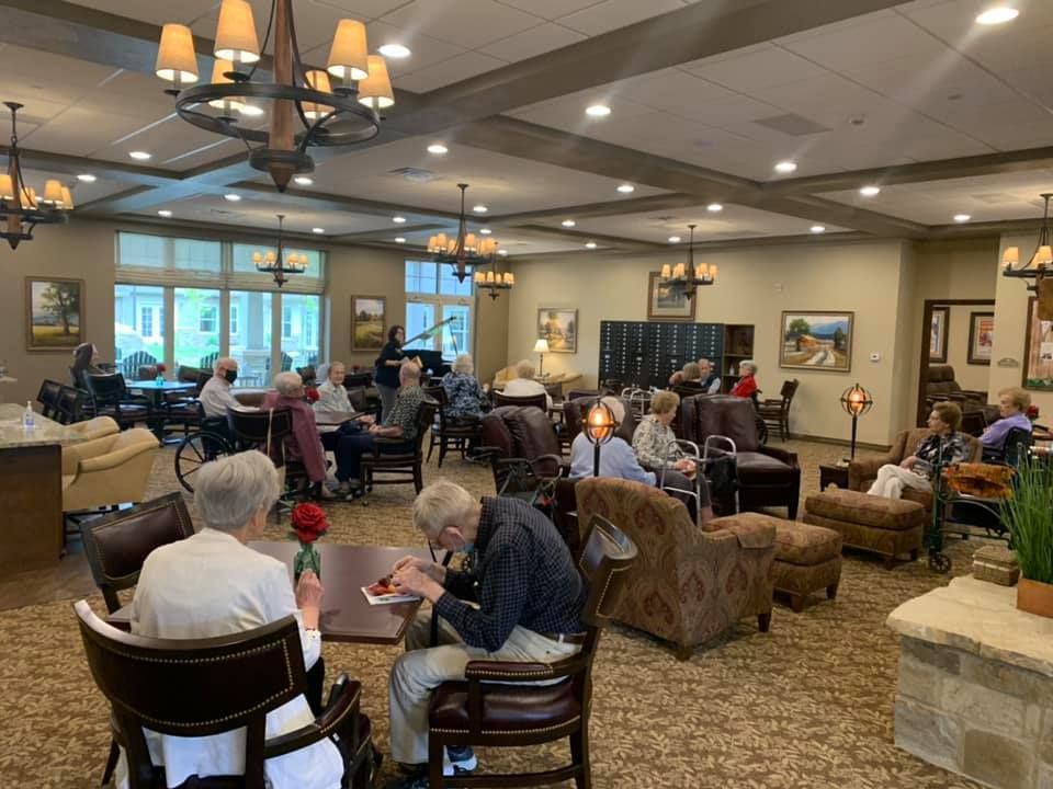 Senior men and women relaxing in the lounge of Springhouse Village East with elegant furniture and chandeliers.