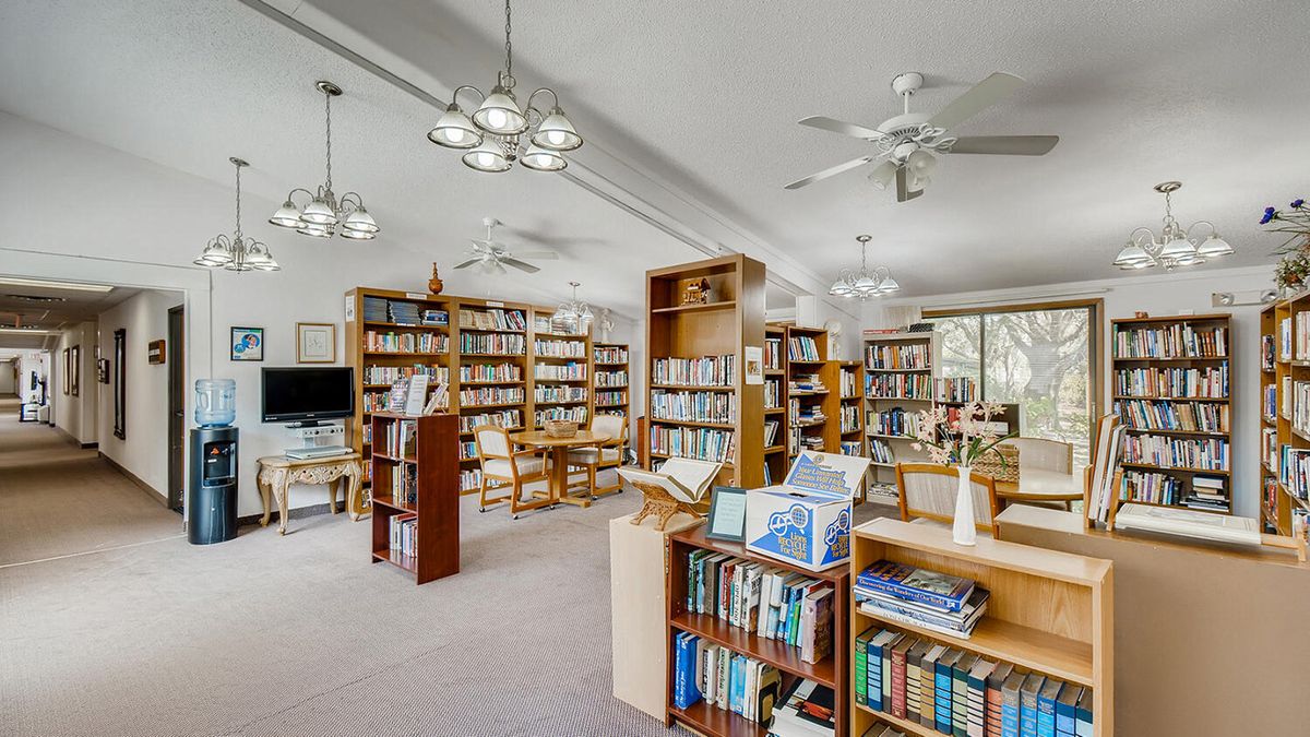 Senior living community library at Woodlands Village with books, furniture, and electronics.