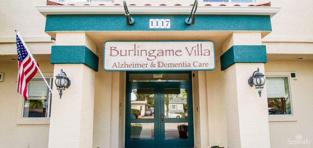 Senior living community, Burlingame Villa, featuring its architectural building, flag, and car transportation.