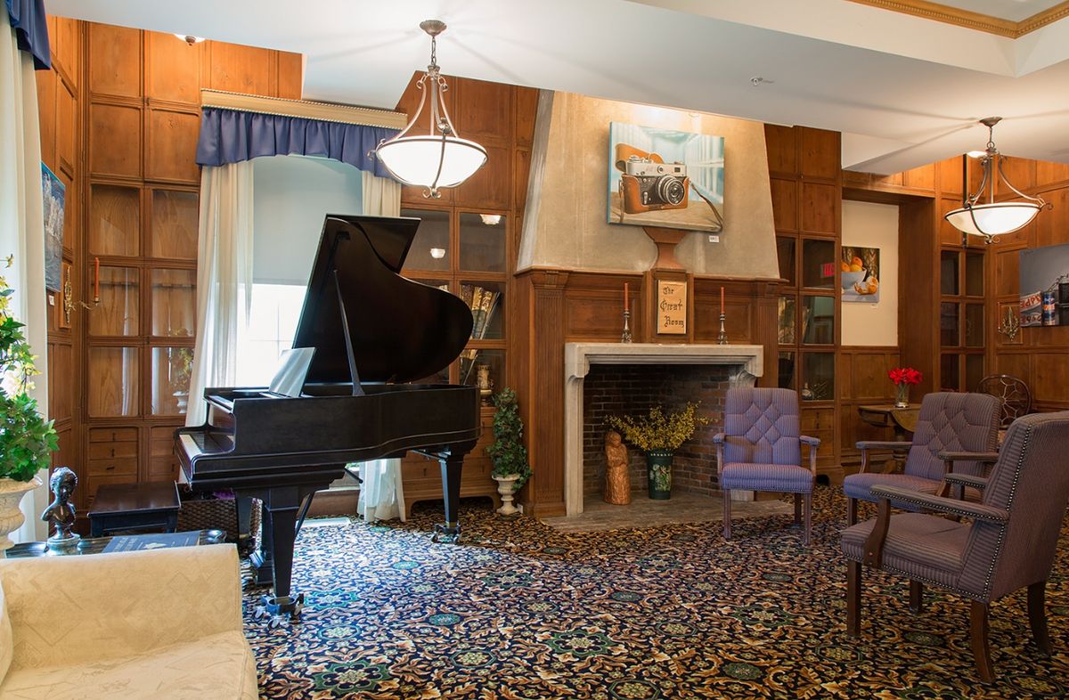 Senior living room interior at Paine Estate featuring grand piano, fireplace, and elegant decor.