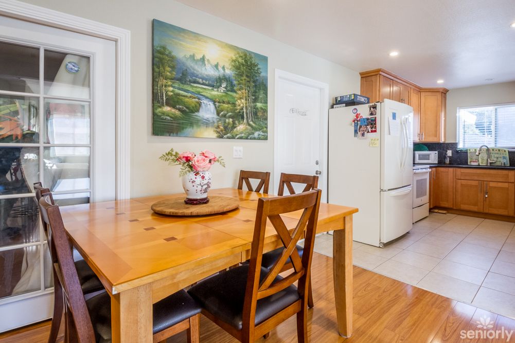 Senior living community interior featuring hardwood flooring, dining room furniture, kitchen appliances, and art.