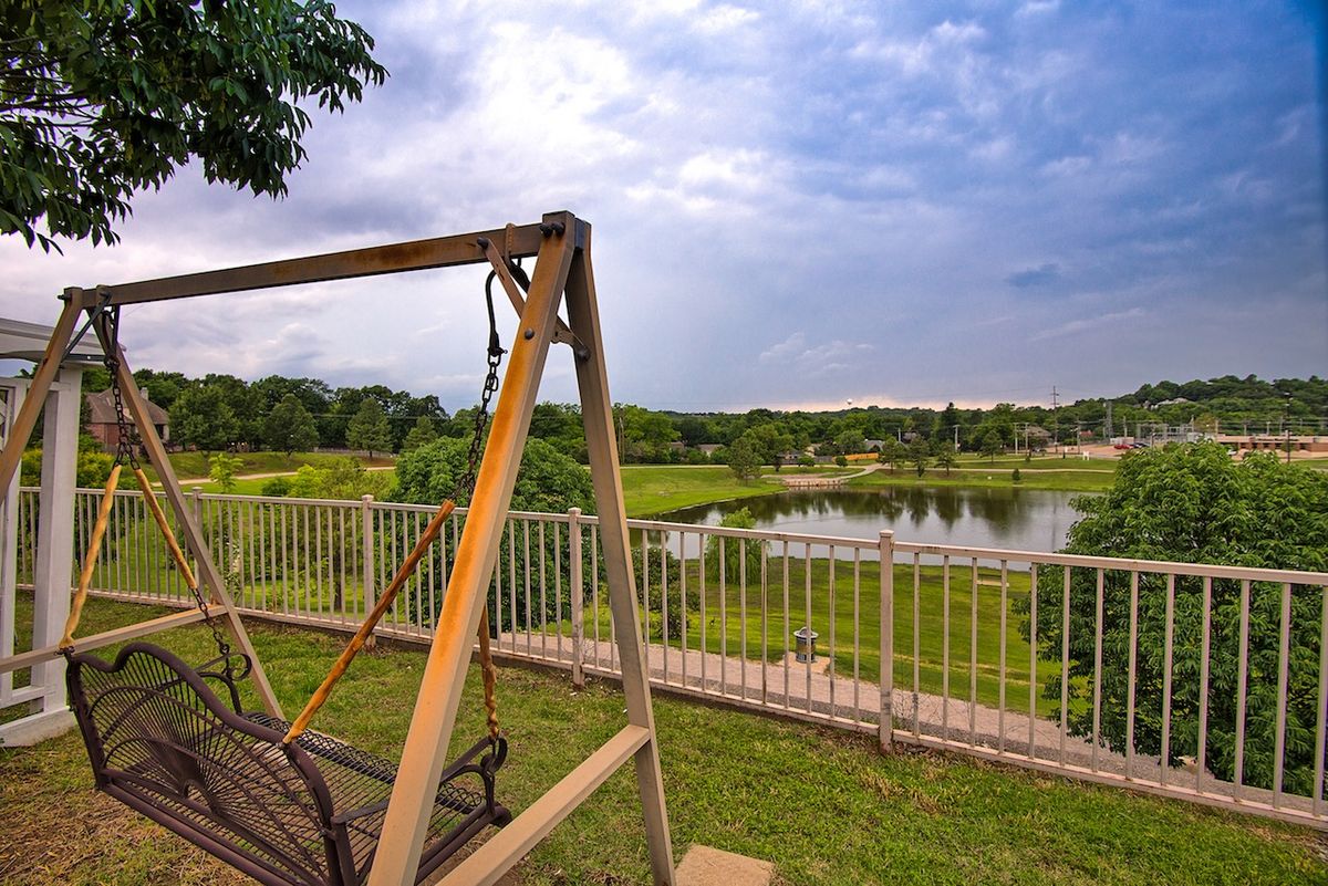 Senior living community in Town Village Tulsa with scenic lakefront, lush greenery, and outdoor swing.