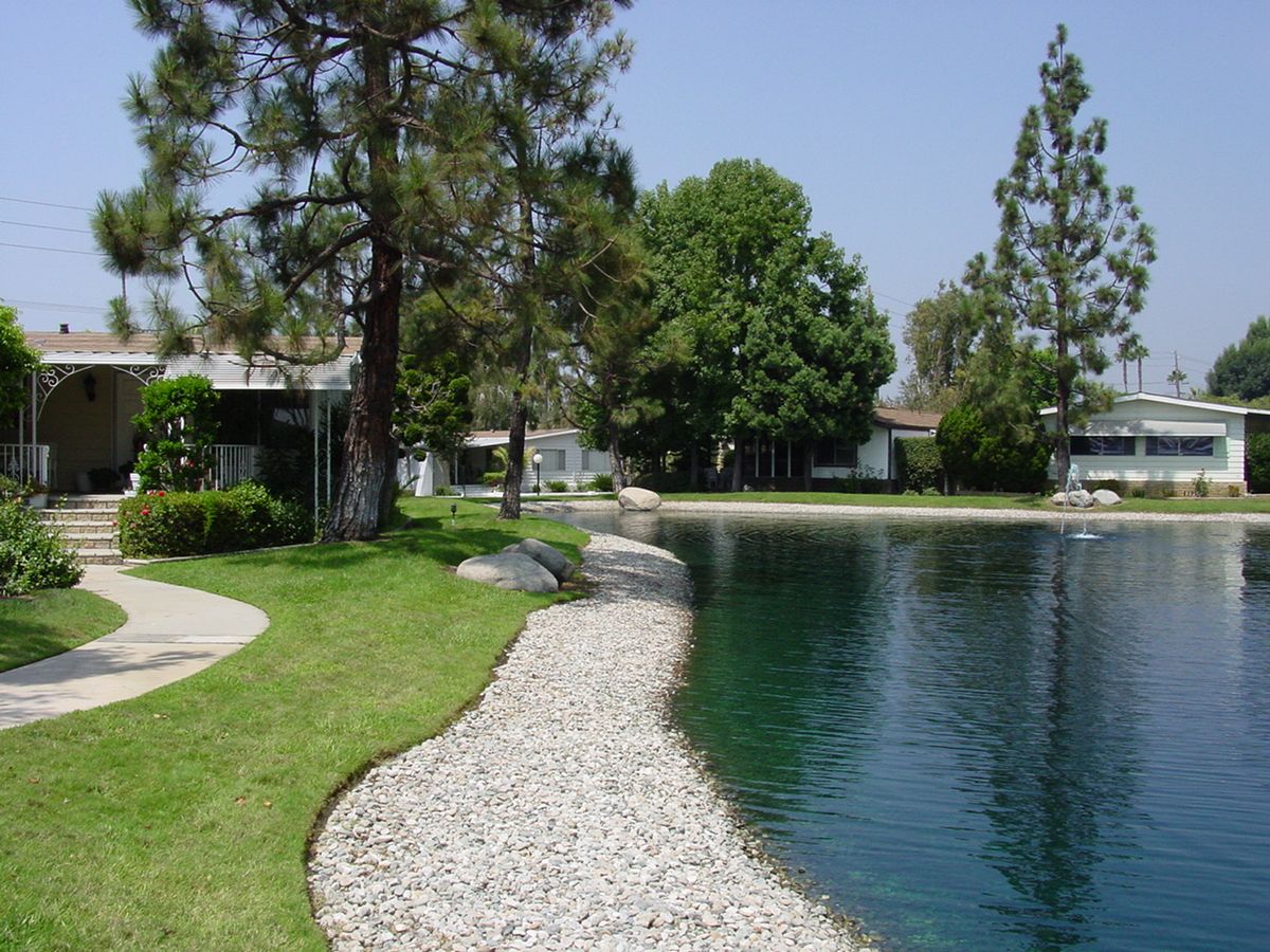 Scenic view of Lake Park La Habra senior living community with lush trees, a lakefront path, and water.