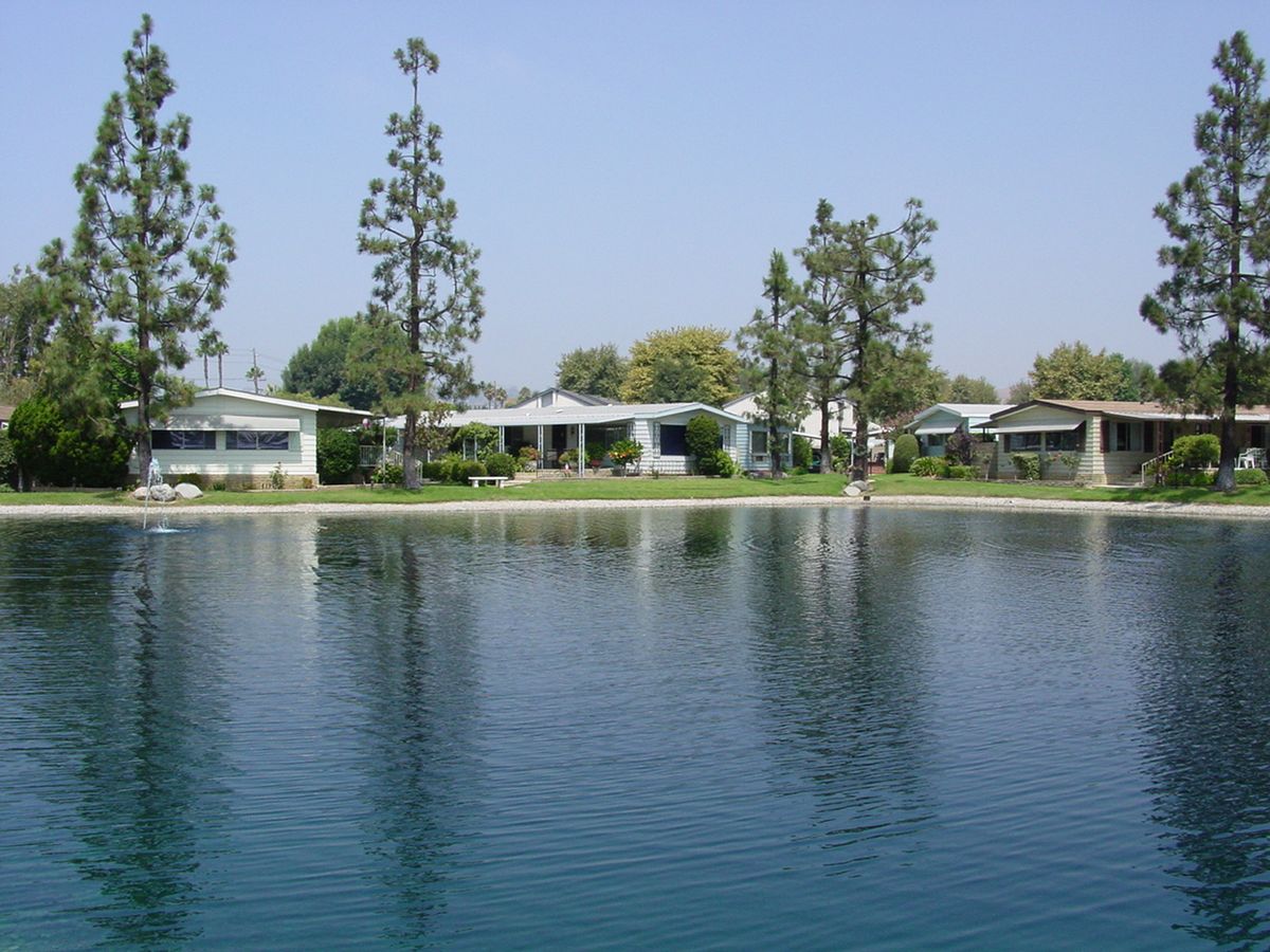 Scenic view of Lake Park La Habra senior living community with lakefront, pool, and lush greenery.