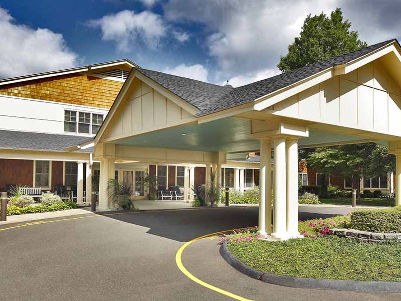 Exterior view of Atria Darien senior living community featuring a portico, outdoor bench, and lush plants.