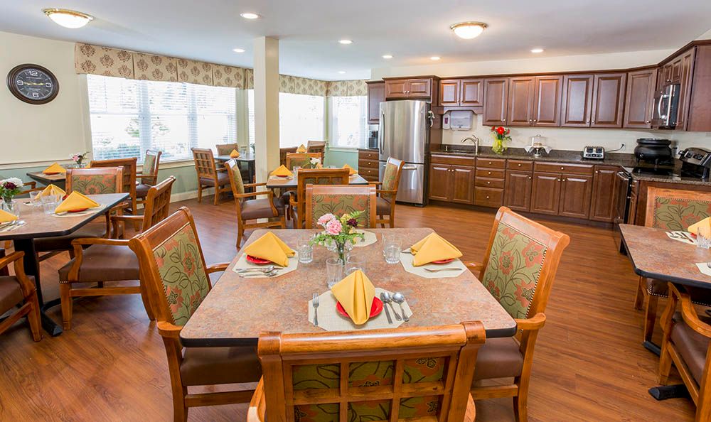 Interior view of Robbins Brook Senior Living featuring dining room with wooden furniture and kitchen appliances.