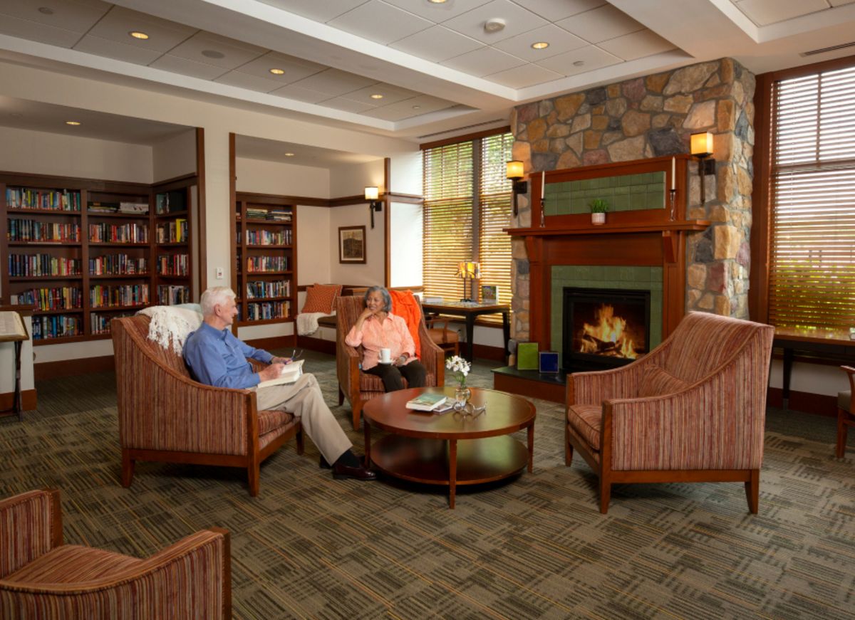 Senior man reading in a cozy living room with fireplace at Waterstone At Wellesley.
