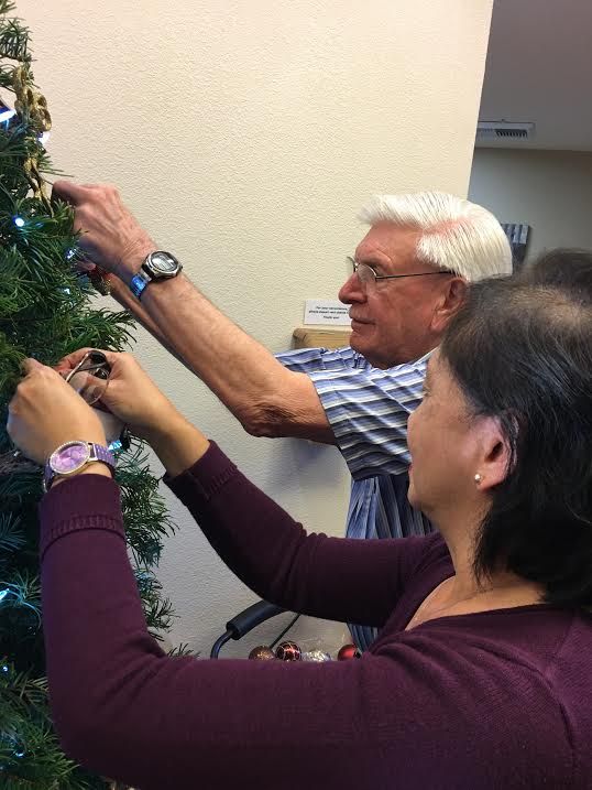 Senior man with glasses at Westmont of Pinole, enjoying Christmas festival with potted plants.