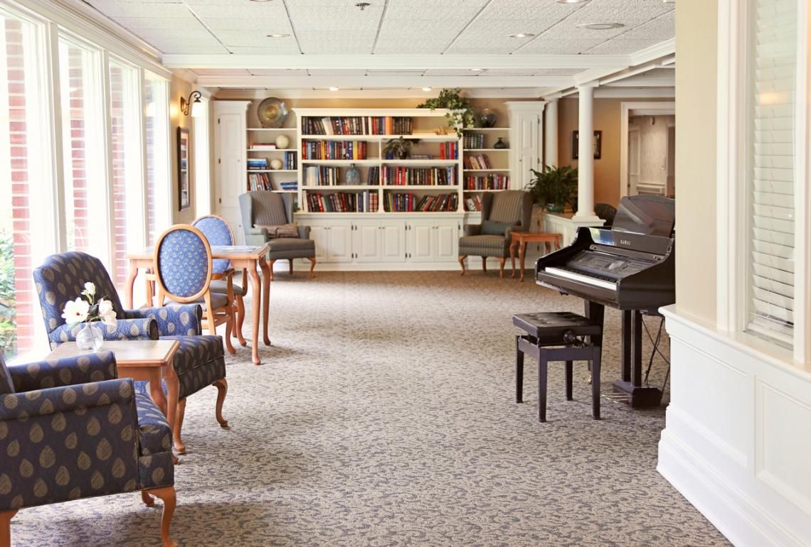 Interior view of Edgewood Centre senior living community featuring a grand piano, library, and elegant decor.