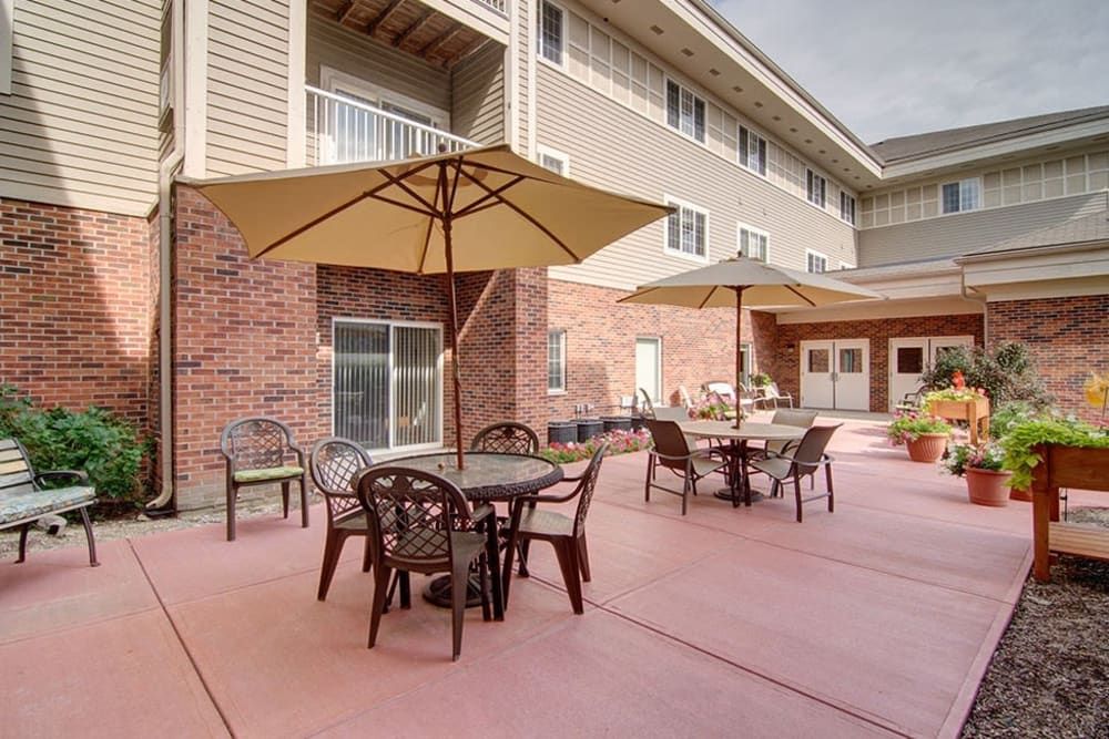 Senior living community patio with chairs, tables, bench, and plants at The Courtyard at McHenry.