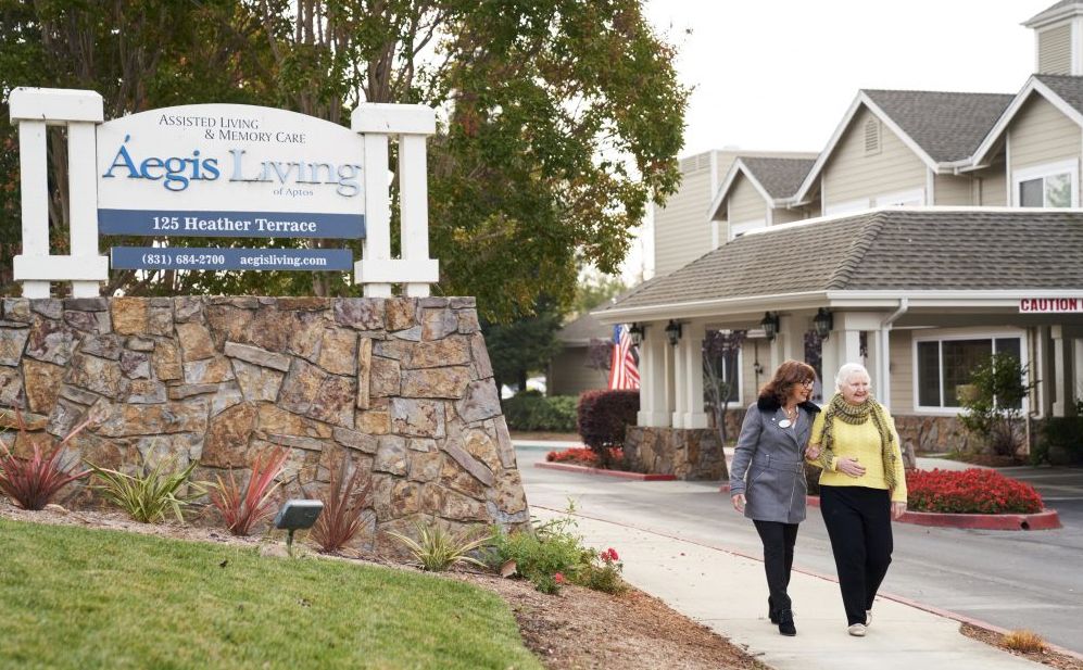 Senior person walking in Aegis Living Greenwood community, showcasing urban architecture and greenery.