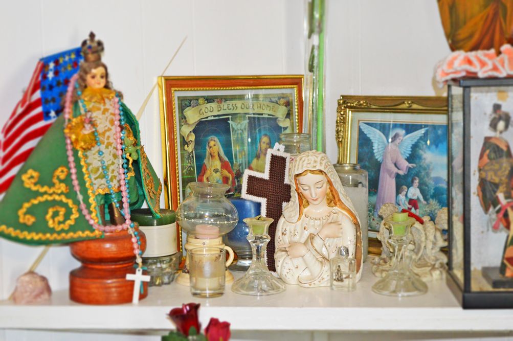 Senior woman praying in church at Nena & Ray's Guest Home, surrounded by flowers and religious symbols.