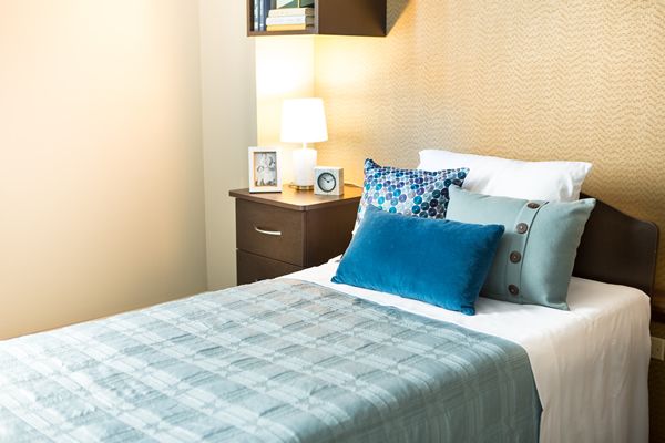 Senior living community bedroom at Lakeshore featuring cushioned furniture, home decor, and lamp.