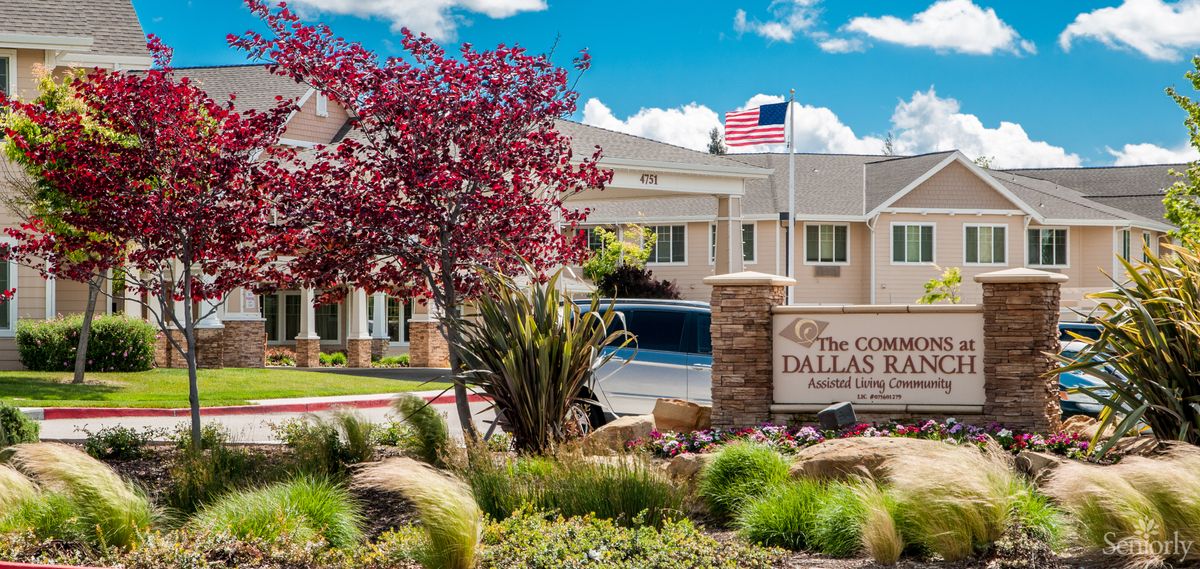 Senior living community, The Commons At Dallas Ranch, featuring lush lawns, trees, flowers, and American flag.