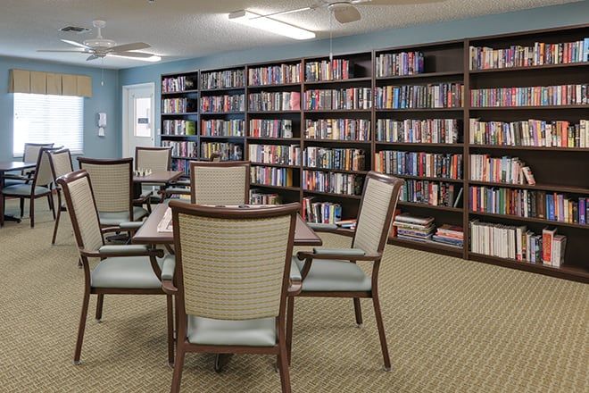 Senior living community library at Brookdale Palma Sola with cozy chairs, lamps, and bookcases.