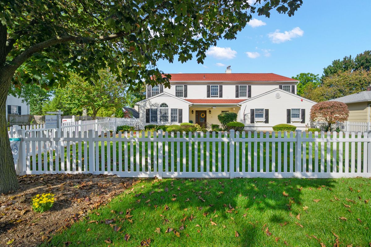 Senior living community, Fox Trail Memory Care at Paramus, featuring a lush yard, outdoor lamp, and picket fence.