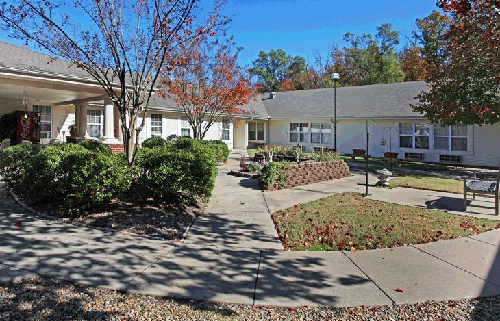 Pathway in Willow Grove, Maumelle's senior living community, featuring lush greenery, houses, and outdoor furniture.