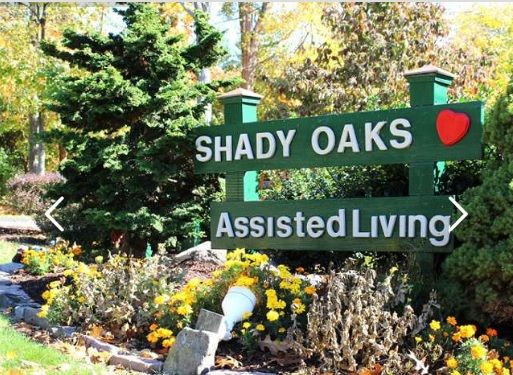 Shady Oaks Assisted Living community surrounded by lush gardens, trees, and wildlife signage.