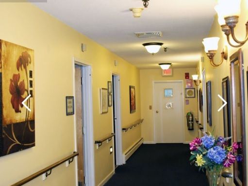 Interior hallway at Shady Oaks Assisted Living with art, plants, and flower arrangements.