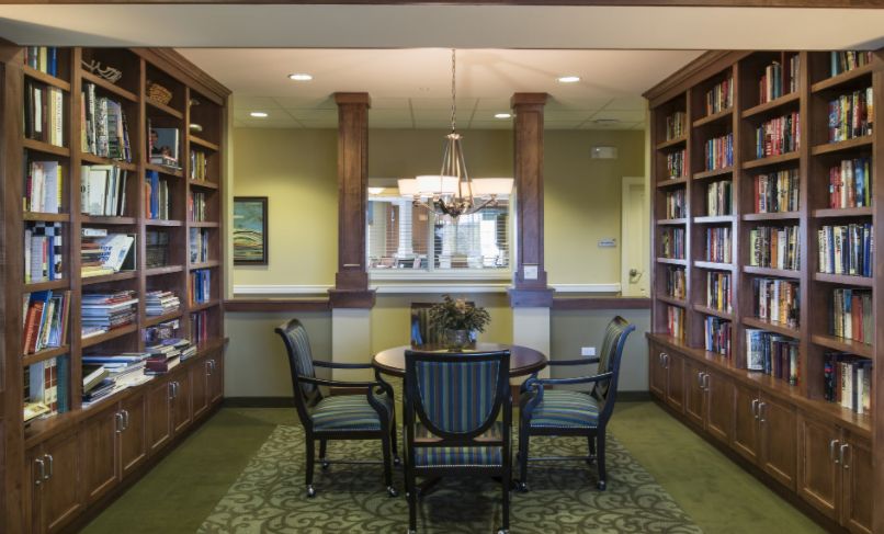 Interior view of Book Lodge senior living community featuring a library with bookcases, furniture, and chandeliers.