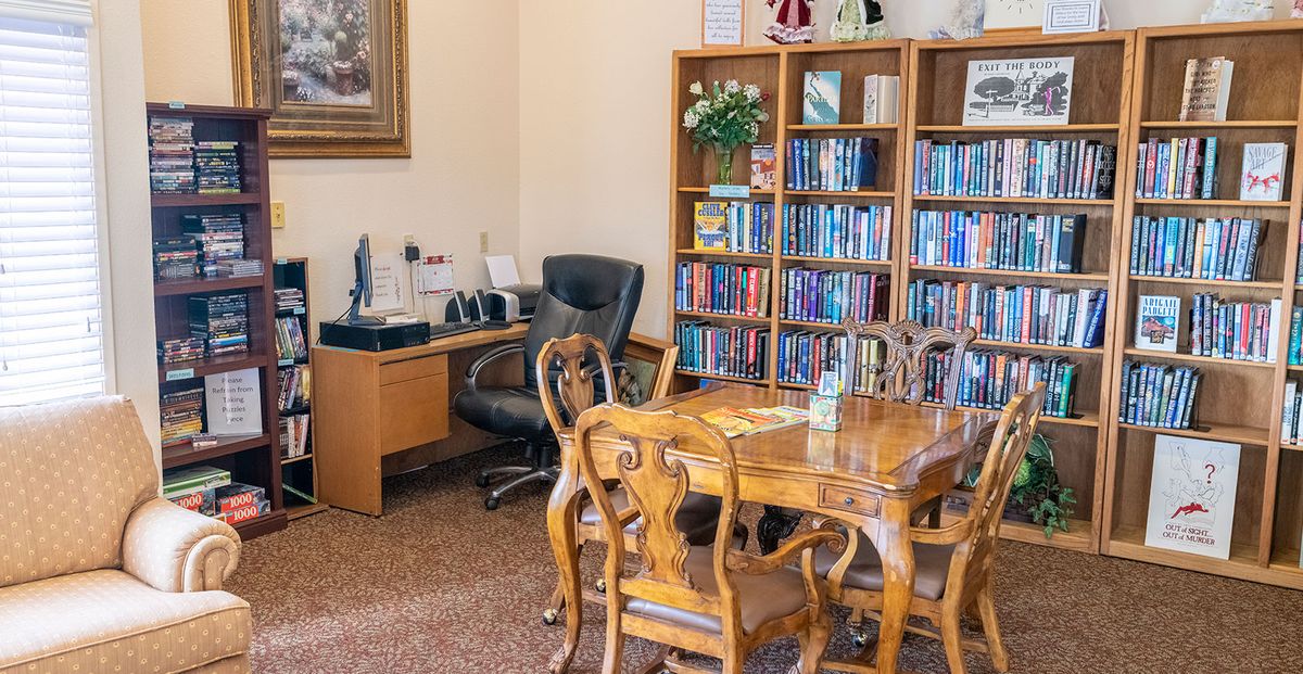 Senior living community library in Camelot with furniture, books, and dining area.