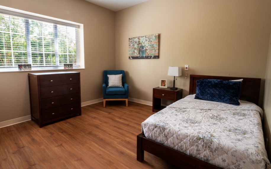 Interior view of a furnished bedroom in Serene Suites senior living community with hardwood flooring.