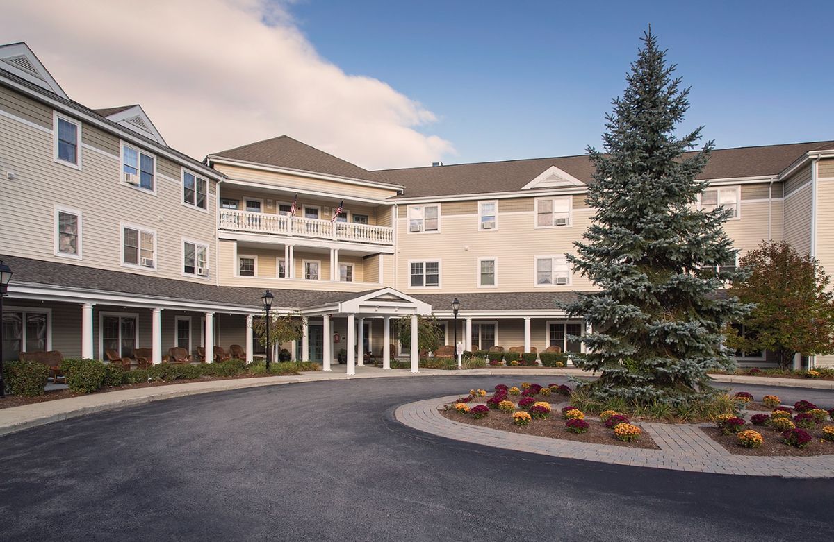 Senior living community in Dedham with urban architecture, pine trees, and outdoor furniture.