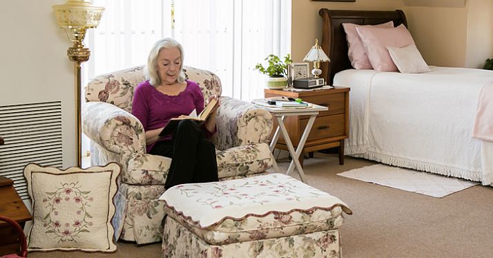 Senior woman reading in a furnished living room at Landmark At Longwood senior community.