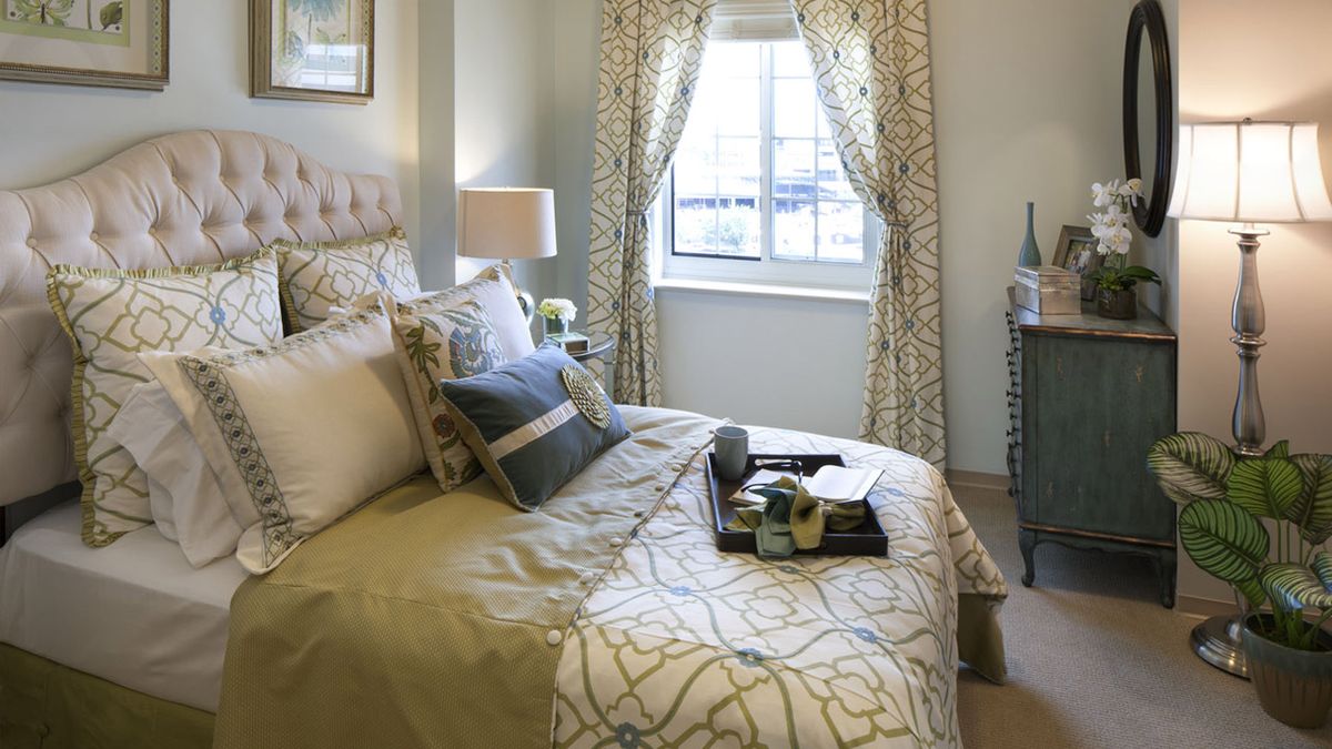 Bedroom interior at Belmont Village Senior Living Cardiff By The Sea with cozy decor and plants.