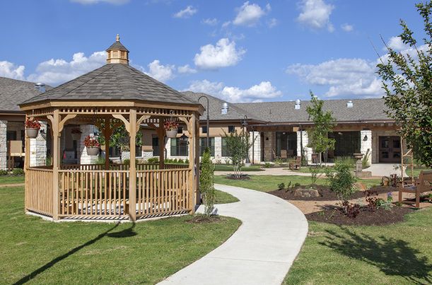 Senior living community, Auberge At Onion Creek, featuring a gazebo, porch, and patio in a lush yard.